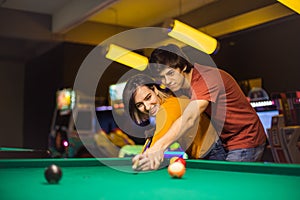 Young couple spending time in billiard room. Boyfriend teaching his girlfriend to playing billiard