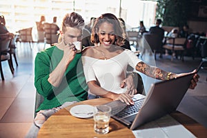 Young couple spending time in cafe watching media to laptop