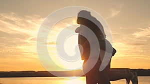 Young couple spinning and dancing at sunset on the beach. Loving man and woman dance on background of lake.