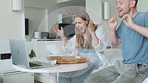 Young couple sport fans watching football match at home and cheering team. Happy friends with pizza watching soccer game