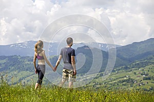 Young couple, sportive man and slim woman holding hands outdoors on background of beautiful mountain landscape on sunny summer day