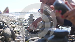 Young couple stacks of stones and sea splash in slow motion on sunny day. 3840x2160