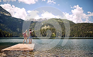 A young couple is standing on the dock at the lake and enjoying the view during mountain hiking. Trip, nature, hiking