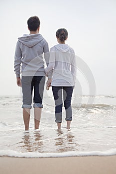 Young couple standing and holding hands on the beach and looking out to sea