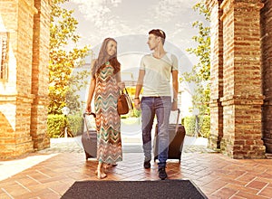 Young couple standing at hotel corridor upon arrival, looking for room, holding suitcases