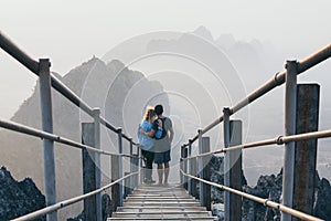 Young couple standing on mountain peak with stairs going down during sunrise foggy morning in Hpa-An, Myanmar