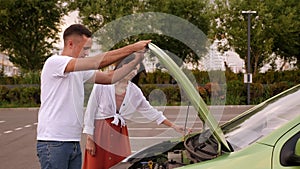 A young couple is standing near a broken car with the hood open.