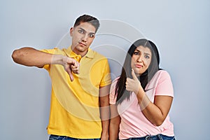 Young couple standing over isolated background doing thumbs up and down, disagreement and agreement expression