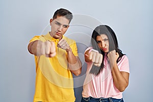 Young couple standing over isolated background punching fist to fight, aggressive and angry attack, threat and violence