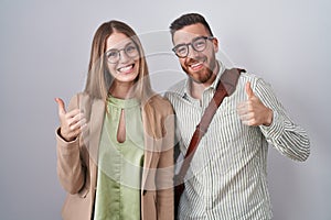Young couple standing over white background doing happy thumbs up gesture with hand