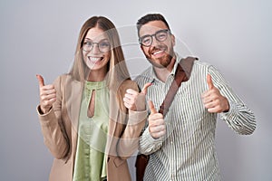 Young couple standing over white background success sign doing positive gesture with hand, thumbs up smiling and happy