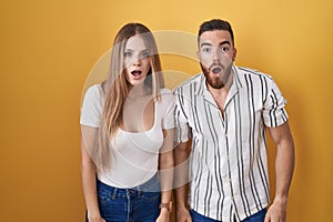 Young couple standing over yellow background afraid and shocked with surprise and amazed expression, fear and excited face