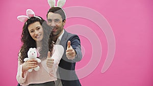 Young couple standing on a pink background. During this show a gesture class smiling and holding a soft toy in the hands