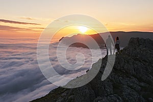 Young couple stands in the mountains above the clouds and looks at beautiful sunset view