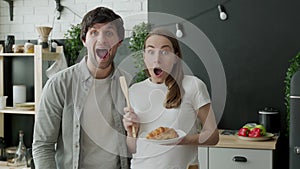 Young couple stared at the camera, standing in surprise in the kitchen at home