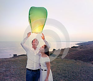 Young couple start a green Chinese sky lantern in the dusk