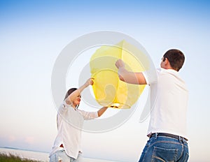 Young couple start a yellow Chinese sky lantern near the sea