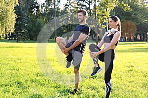 Young couple stretching their legs together while working out at park outdoors