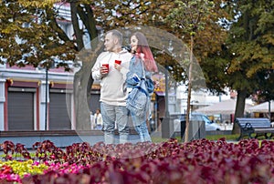 A young couple of students in love - a beautiful girl and a nice guy on the street with cups of coffee in the summer.