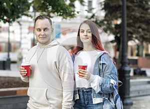 A young couple of students in love - a beautiful girl and a nice guy on the street with cups of coffee in the summer.