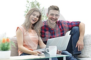 Young couple of students uses a laptop sitting on sofa