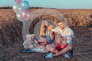 A young couple summer sitting in wheat field. Romantic evening, outdoor recreation. The concept of love music guitar