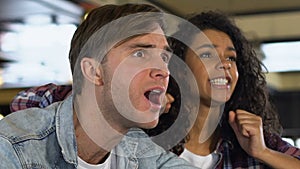 Young couple supporting sports team in pub, disappointed about conceding penalty