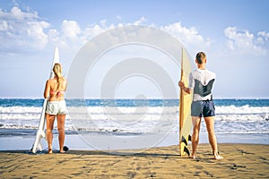 Young couple of surfers standing on the beach with surfboards preparing to surf on high waves