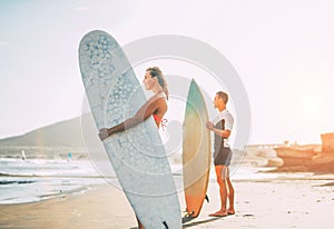 Young couple of surfers standing on the beach with surfboards preparing to surf on high waves during a magnificent sunset