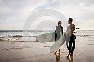 Young couple of surfers walk with surfboards on the beach at sunset