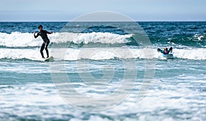 Young couple surfing with surfboard on waves in Atlantic ocean