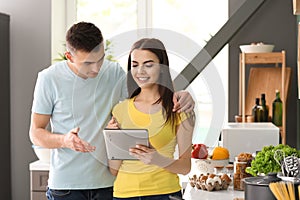 Young couple with tablet PC reading recipes in kitchen