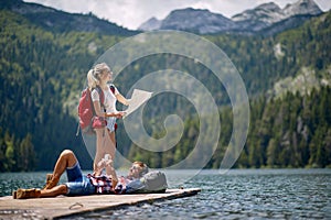 A young couple is taking a rest on the dock at the lake during mountain hiking. Trip, nature, hiking