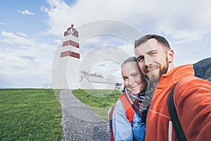 Young couple taking selfie with Alnes lighthouse on background. Godoy island, Norway photo