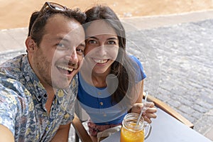 Young couple taking a selfie with smart phone while drink a smoothy and a coffee. Husband and Wife laughing, sitting in a bar.