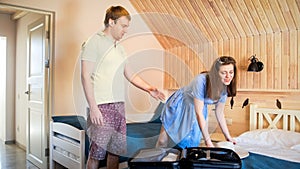 Young couple talking while packing thing in suitcase for their summer vacation