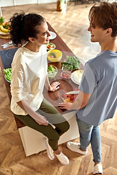 Young couple talking and smiling while preparing healthy meal in the kitchen together. Vegetarianism, healthy food