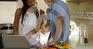 Young couple talking while using laptop in kitchen