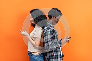 Young Couple Texting On Smartphones Against Orange Background