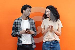 Young Couple Texting on Smartphones Over Orange Background