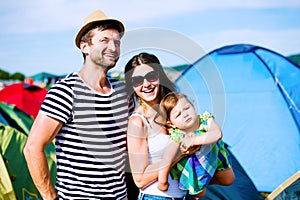 Young couple with their baby daughter between tents, summer