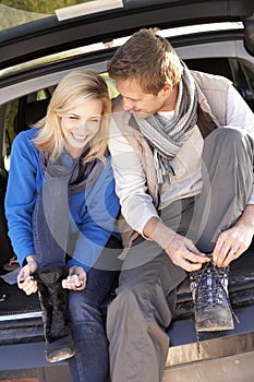 Young couple tie boots at rear of car