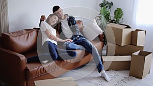 Young couple is tired after moving in their new house and resting on sofa. Girl leaning on her boyfriend, exhaling