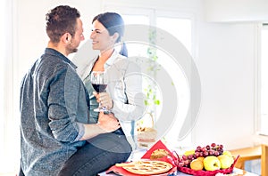 Young couple toasting red wine on tender moment at home kitchen - Happy millenial lovers enjoying relax moment cheering together
