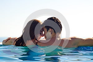 Young Couple Together in an Infinity Swimming Pool. Rear View of Honeymoon Couple at Luxury Resort. Travel and Summer Vacation.