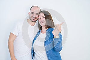 Young couple together over white isolated background smiling with happy face looking and pointing to the side with thumb up