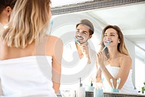 Young couple with toothbrushes near mirror in bathroom.