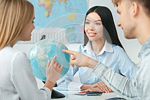 Young couple in a tour agency communication with a travel agent travelling concept globe choosing destination