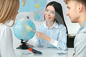 Young couple in a tour agency communication with a travel agent travelling concept globe showing destination