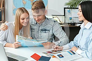 Young couple in a tour agency communication with a travel agent travelling concept holding booklet